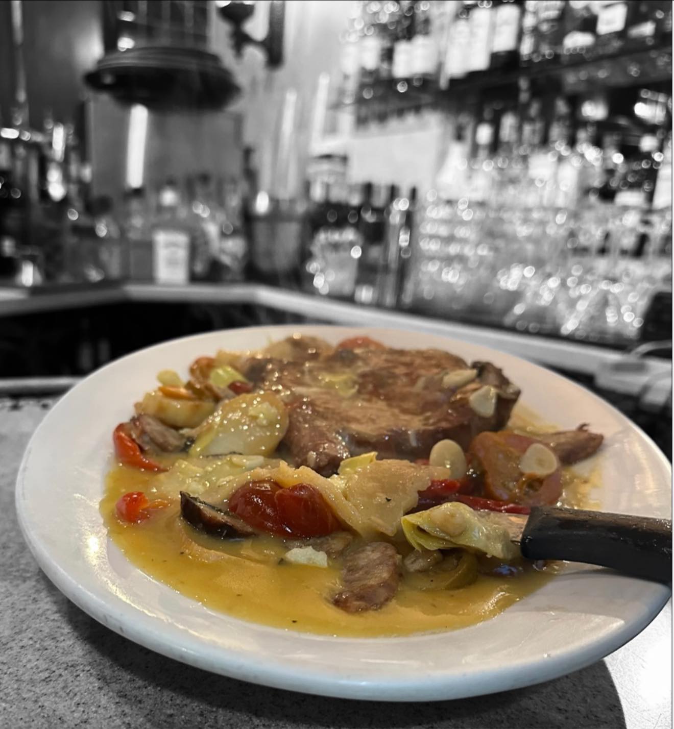 A plate of meat, vegetables, and sauce at a restaurant bar.