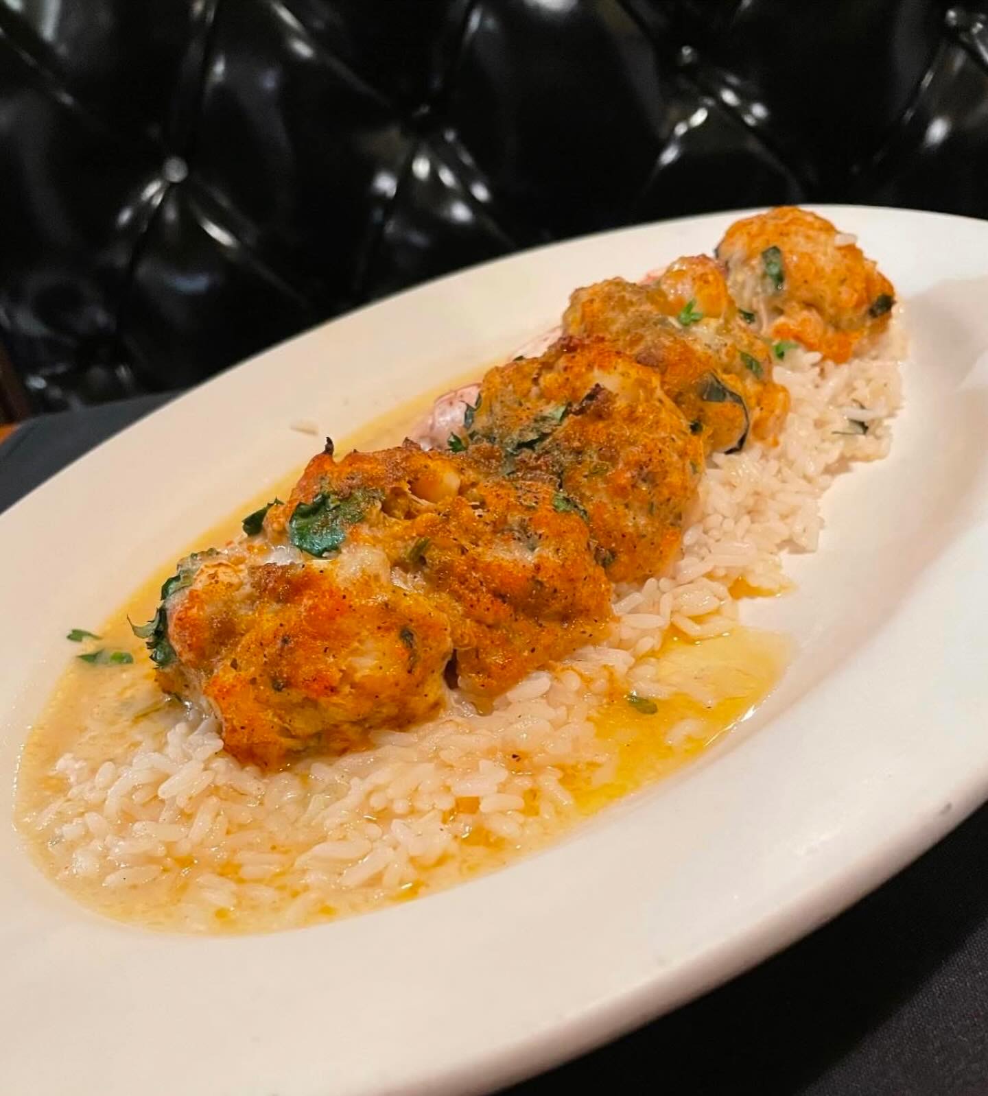 Five orange-brown savory balls on white rice with sauce.