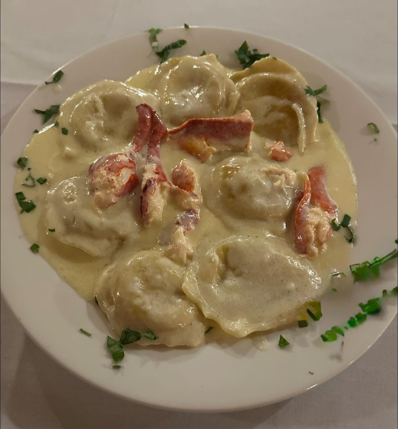 Lobster ravioli with creamy sauce and green herb garnish.