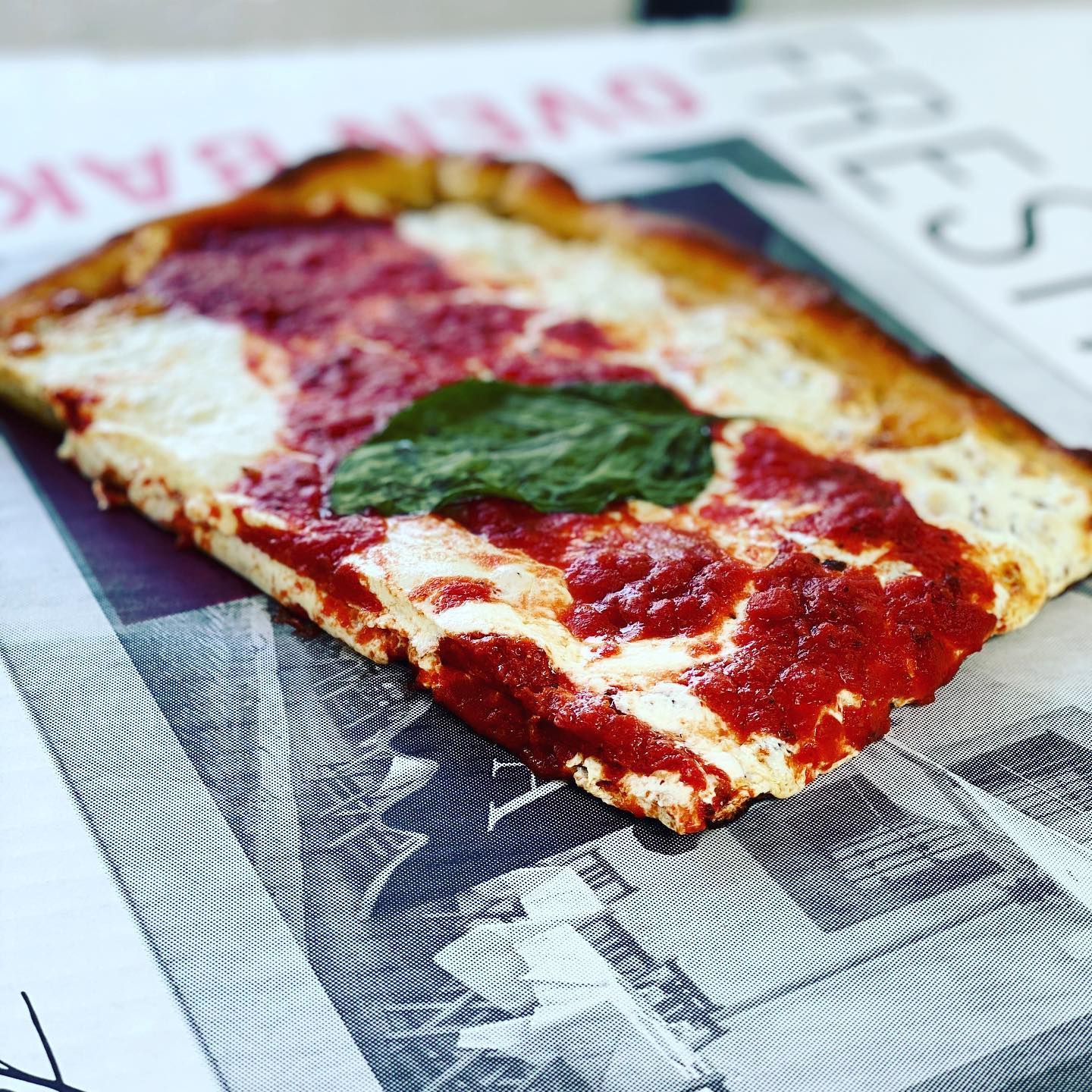 Rectangular pizza slice with red sauce, white cheese, and basil.