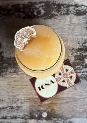 An icy cocktail with a dried lime slice on an IONA coaster.