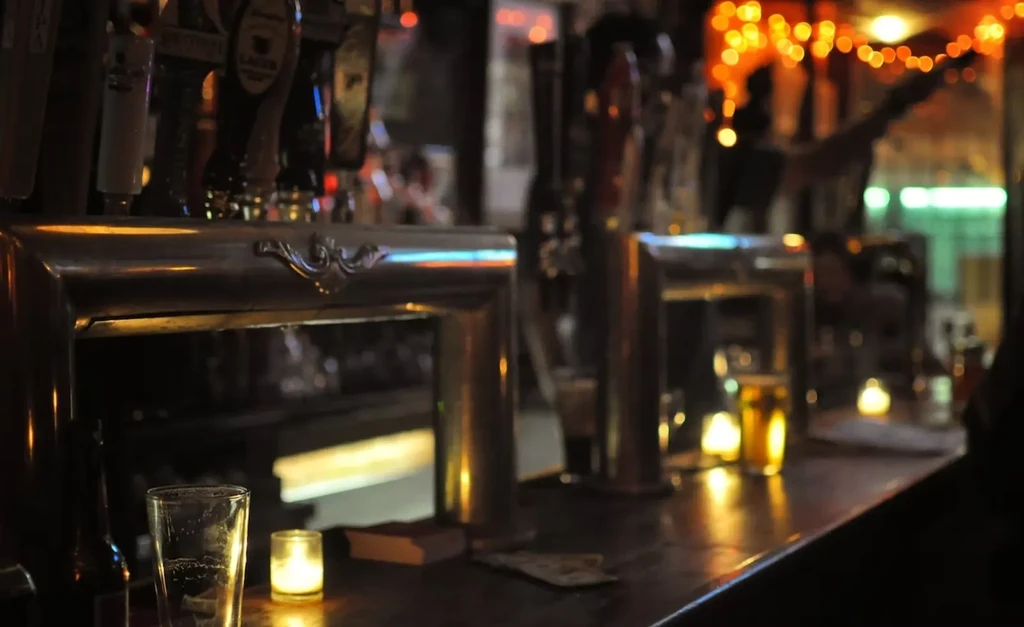 A dimly lit bar counter with beer taps, candles, and empty glasses.