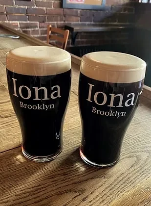 Two glasses of dark beer with white foam on a wooden bar.