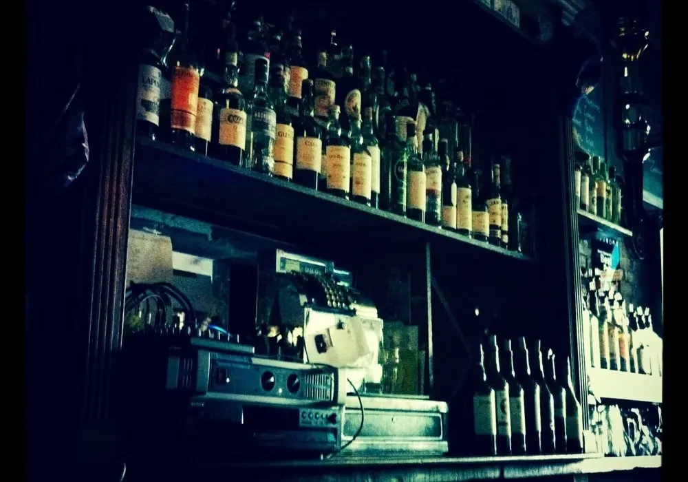 A dimly lit bar with rows of liquor bottles and a vintage cash register.