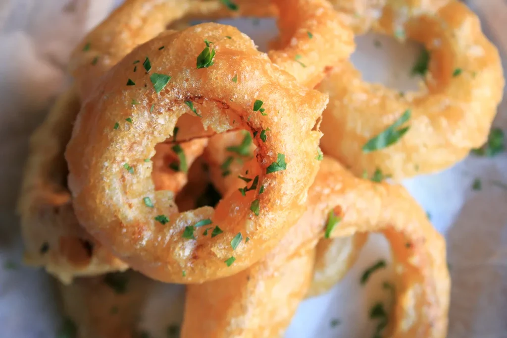 A close-up of golden brown onion rings sprinkled with green herbs.
