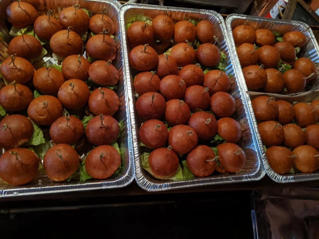 Three foil trays filled with mini burgers on lettuce leaves.