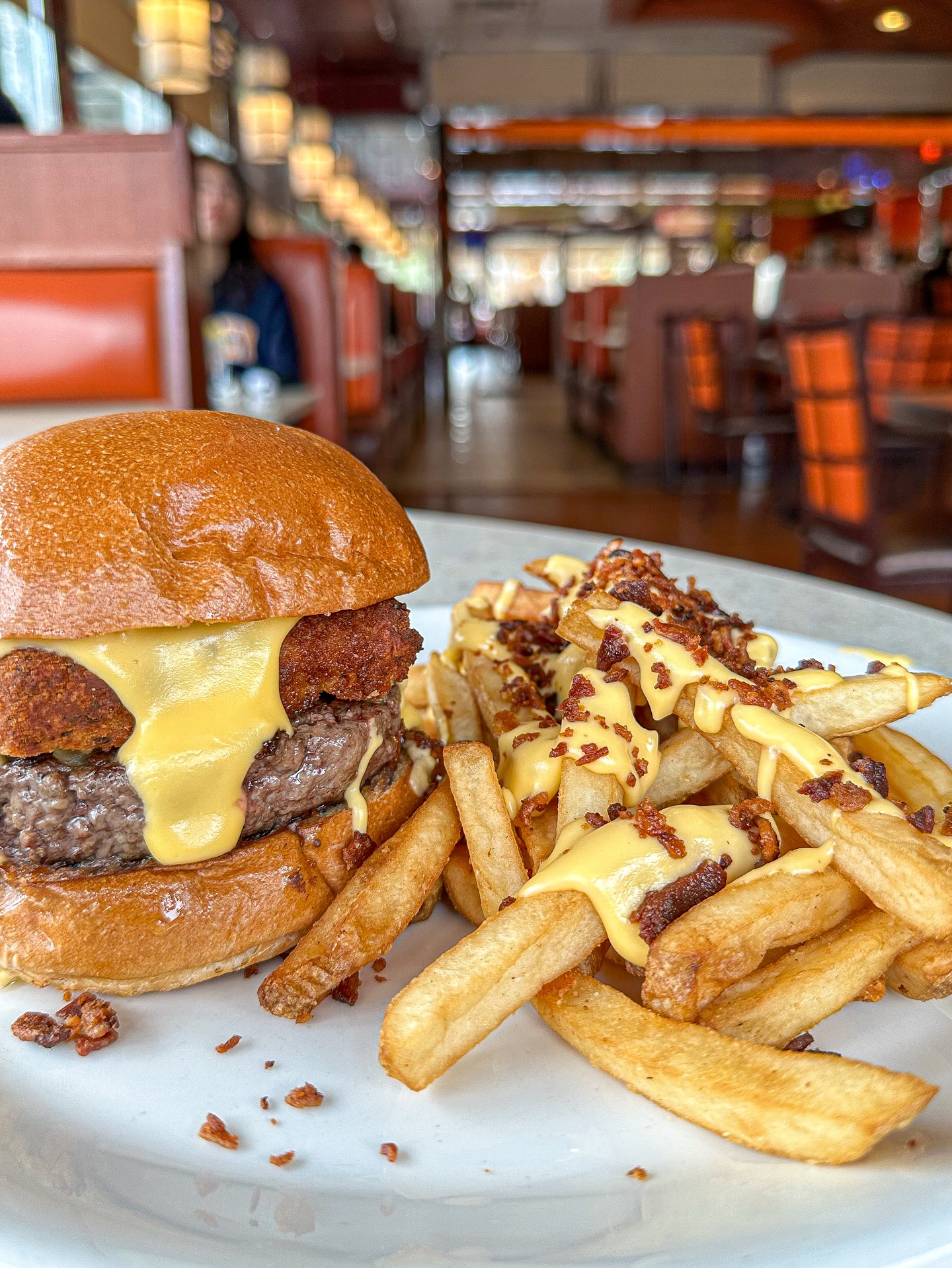 Cheeseburger with fried toppings and loaded cheese fries in a diner.