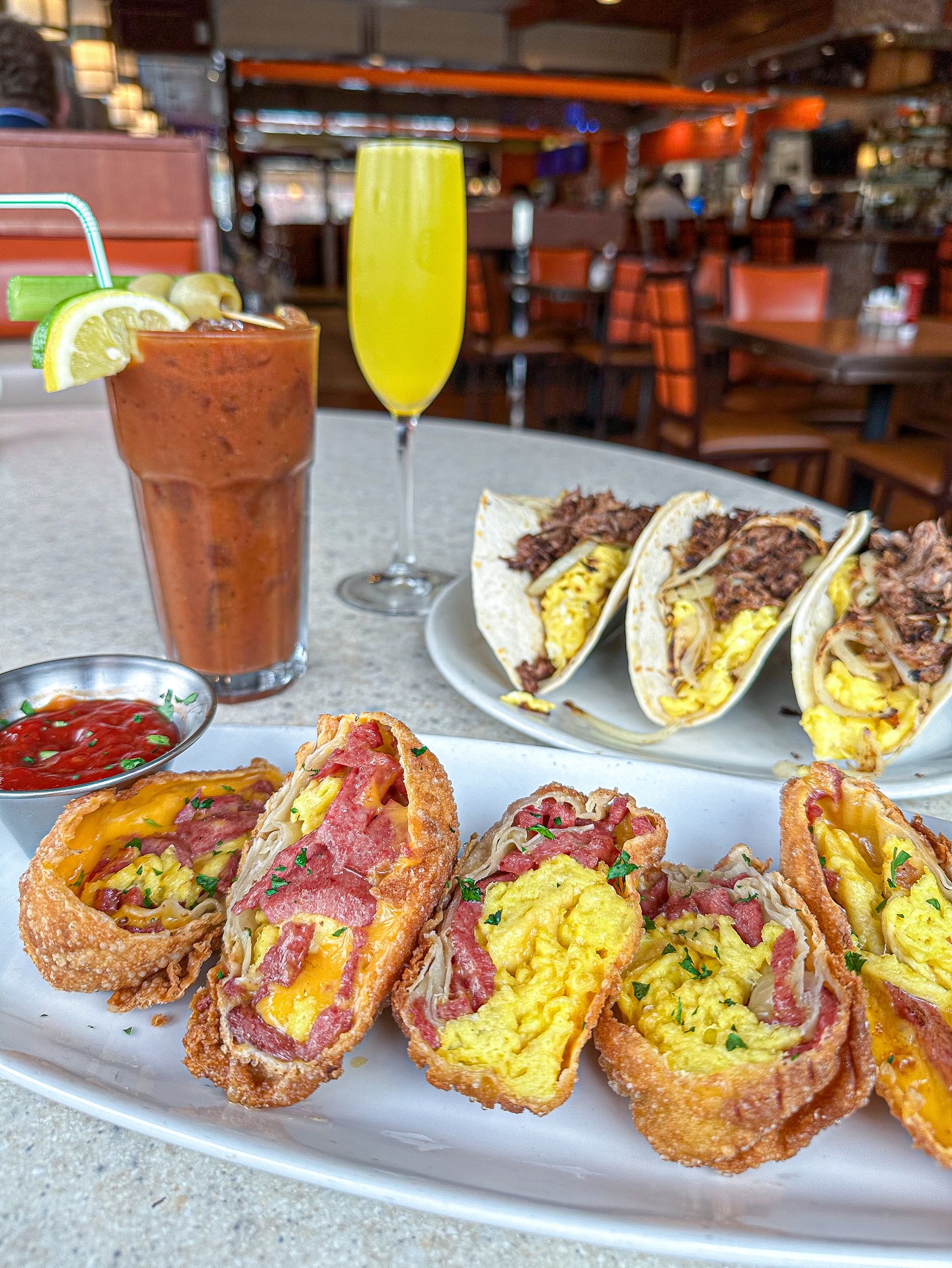 Breakfast egg rolls, tacos, Bloody Mary, and mimosa at restaurant.