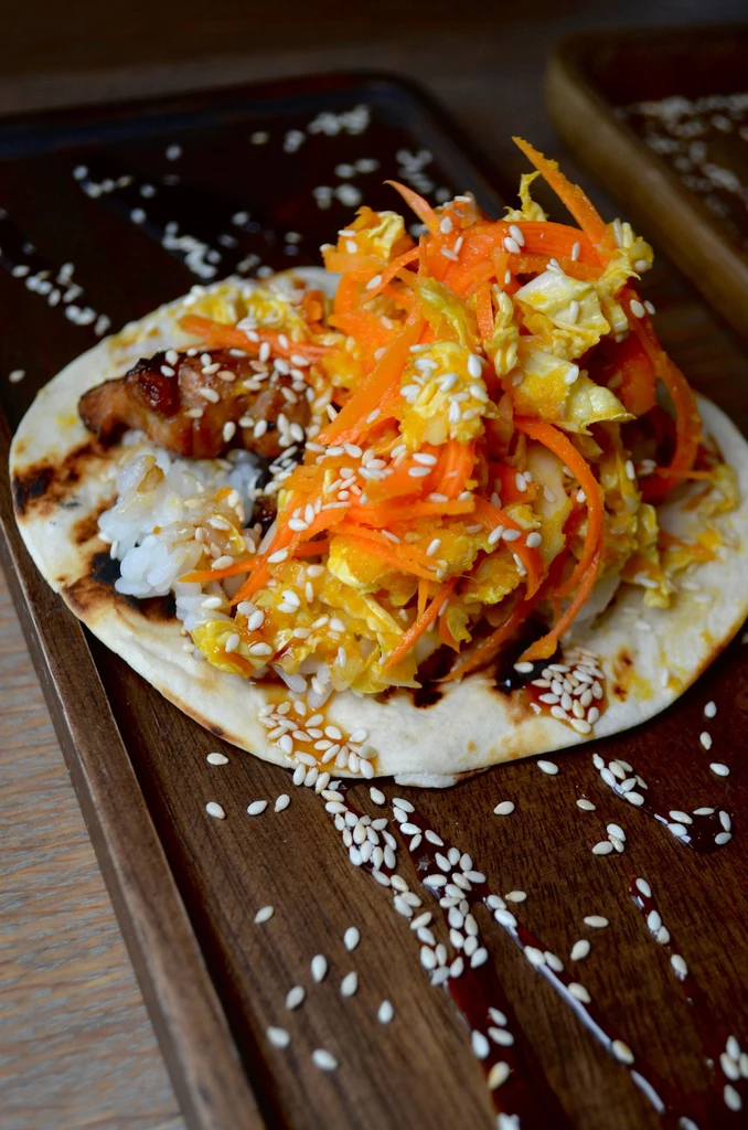 A teriyaki pork taco with rice and coleslaw on a wooden tray.