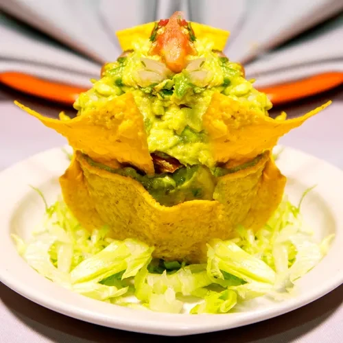 Guacamole with tortilla chips and shredded lettuce on a white plate.
