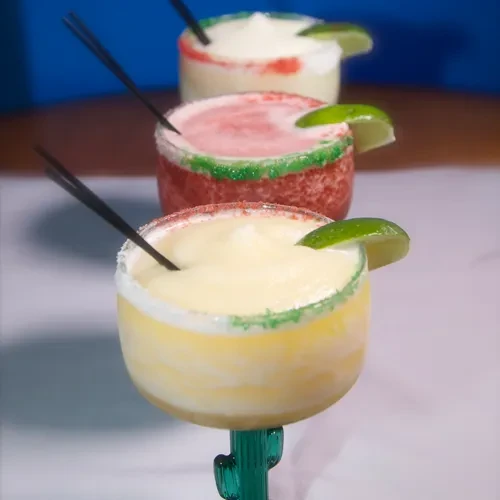 Three colorful frozen margaritas in decorative glasses, garnished with lime.