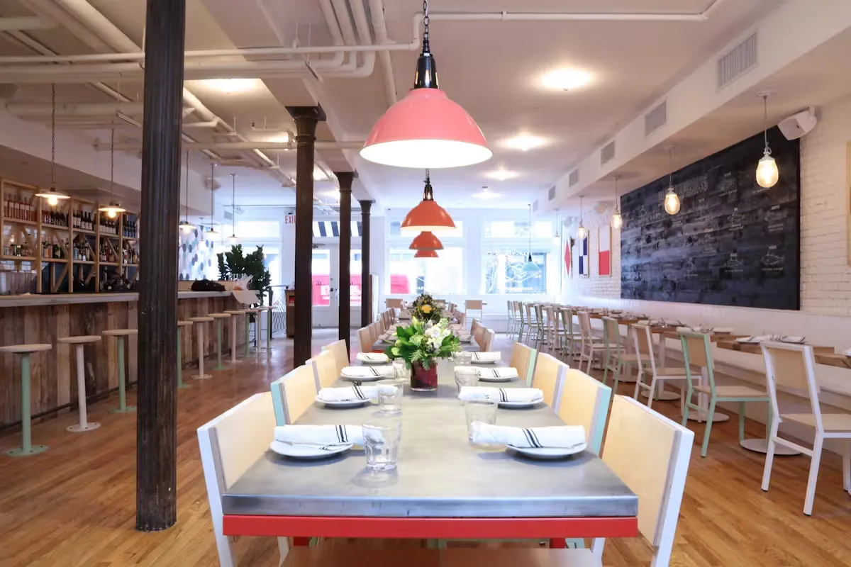 A modern restaurant with long tables, exposed beams, and a bar area.