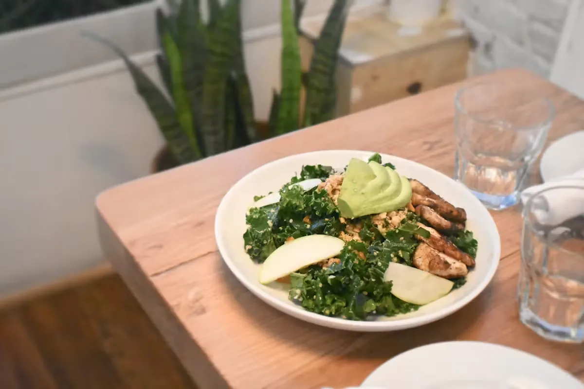 Kale salad with chicken, avocado, apple slices, and nuts.