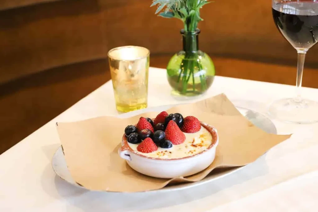 Dessert dish with berries on white table with drink and candle.