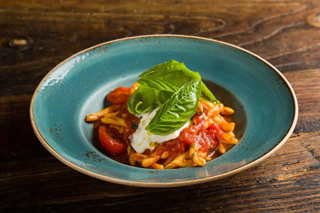 Pasta with red sauce, fresh tomatoes, mozzarella, and basil in a blue bowl.