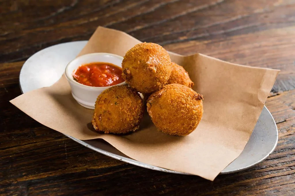 Four golden-fried arancini balls with a side of marinara sauce.
