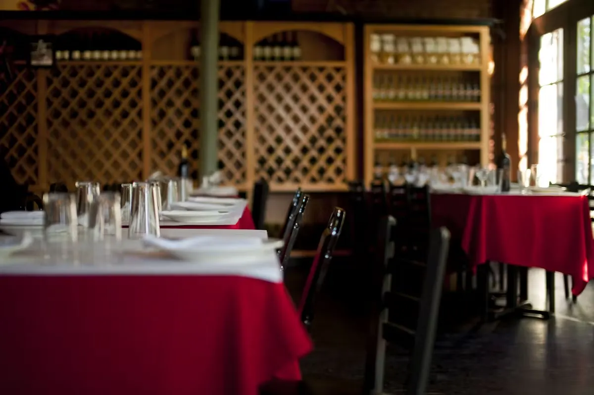 Empty restaurant with tables set with red tablecloths and wine racks.