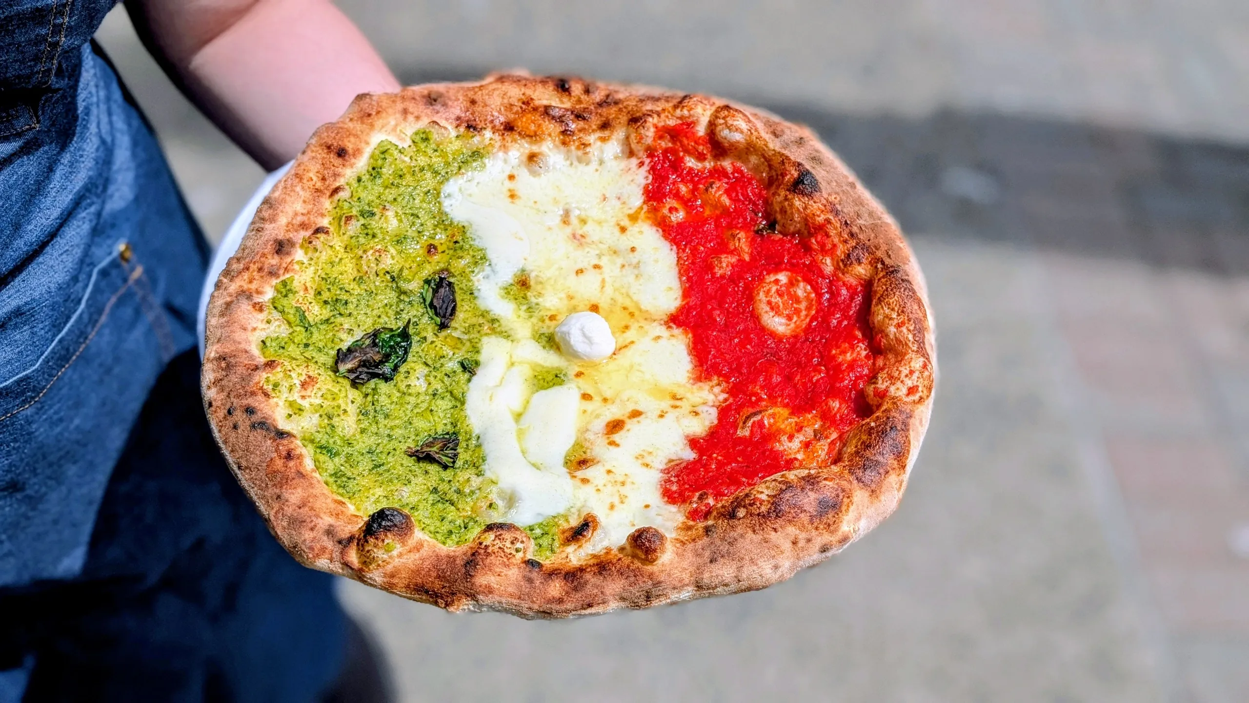 A person holds a pizza with toppings colored like the Italian flag.