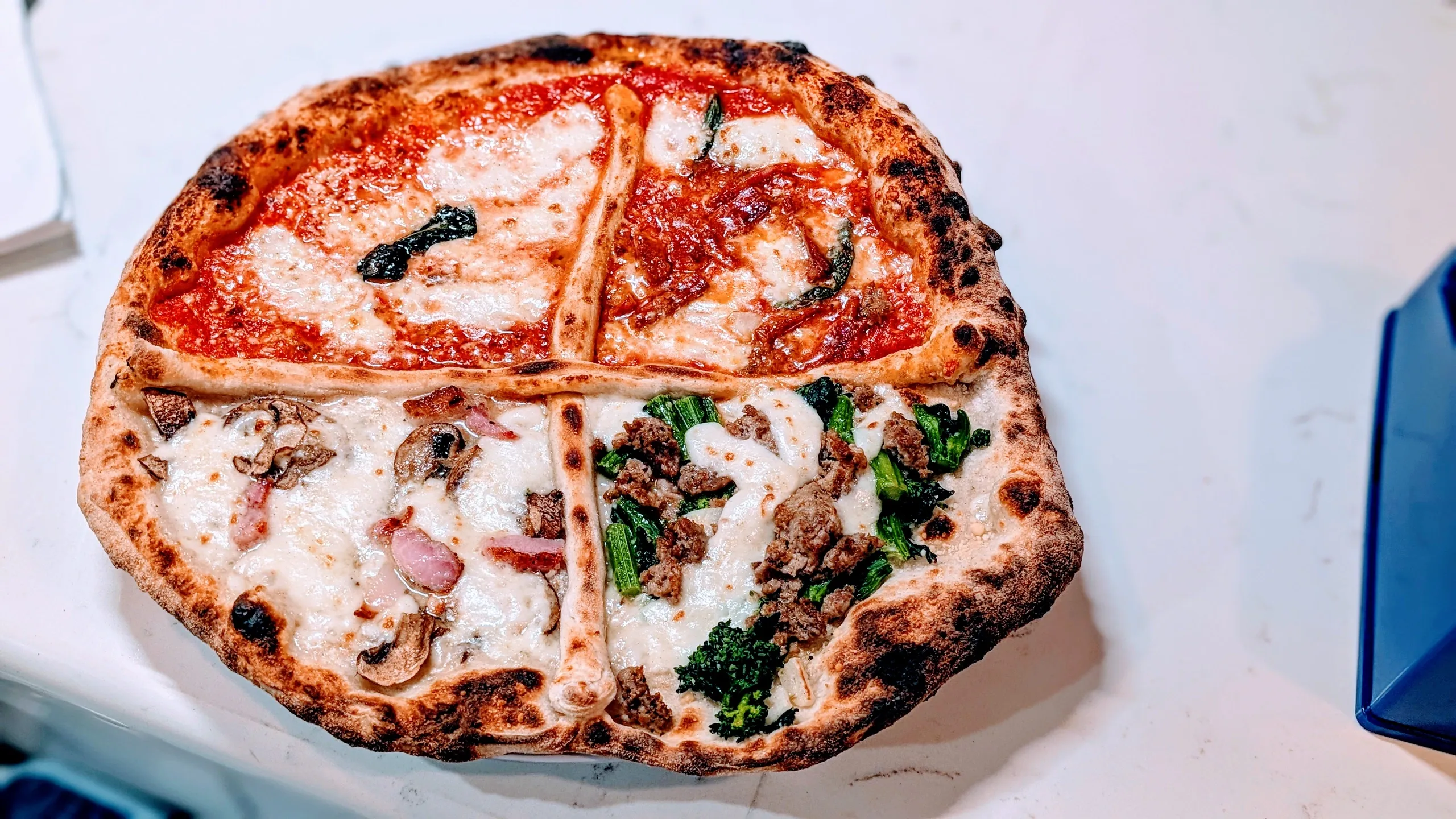 A four-section pizza with various toppings on a white surface.