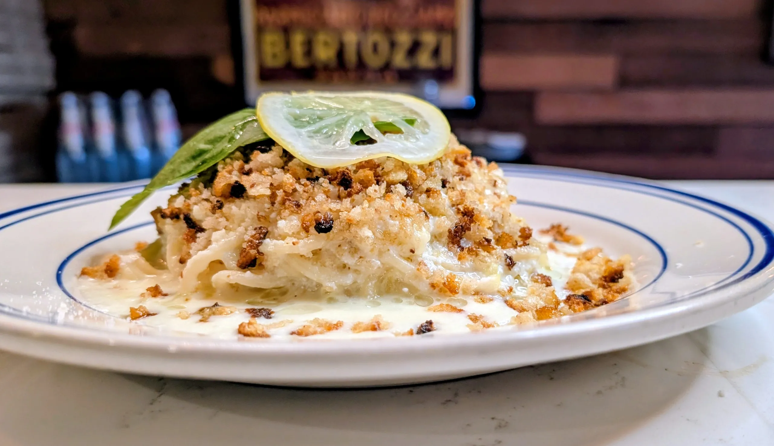 Pasta dish with breadcrumbs, lemon slice, and basil on a white plate.