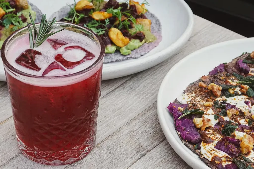 A red drink with rosemary next to two purple tortilla dishes.