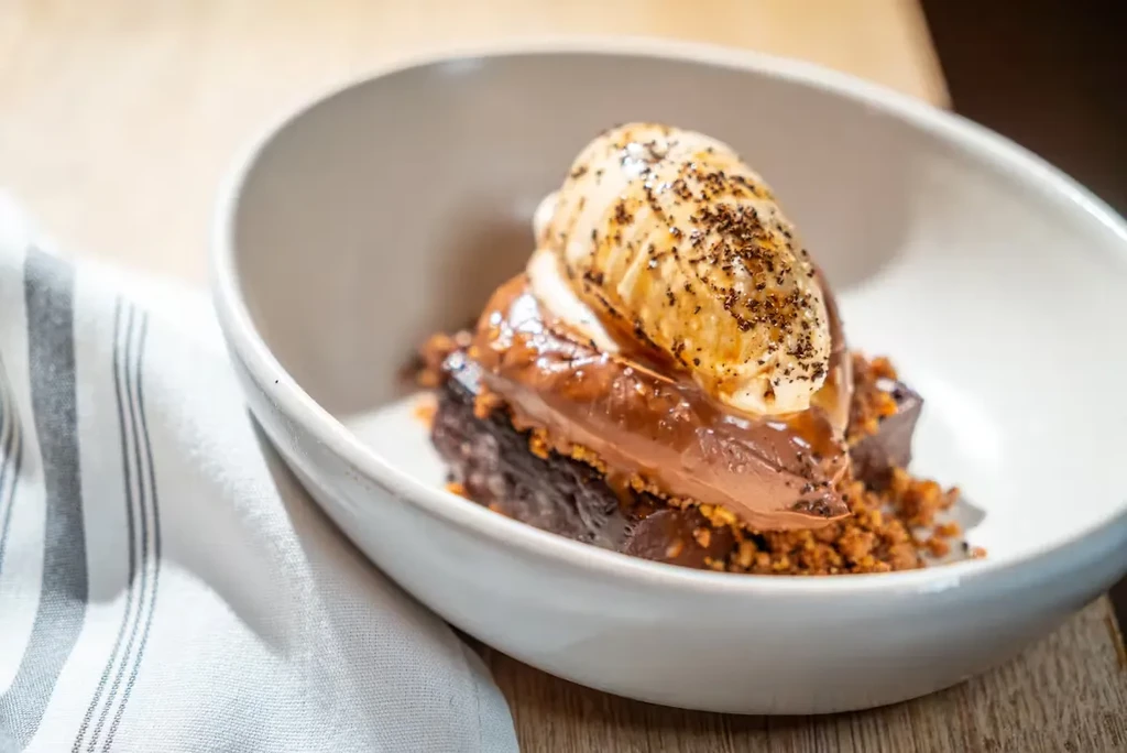 Chocolate dessert with ice cream and crumbled topping in a white bowl.