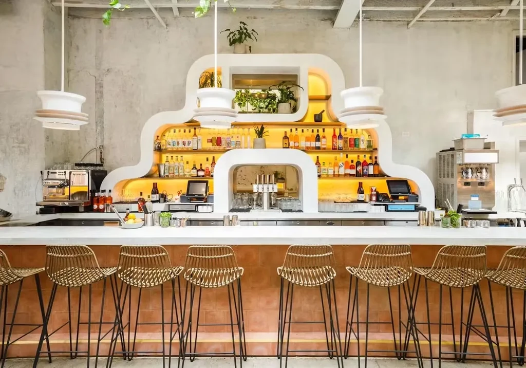 Modern bar with arched shelves, illuminated bottles, and rattan bar stools.