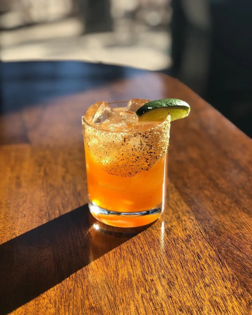 A margarita-like drink with a chili-salt rim and lime wedge on a wooden table.