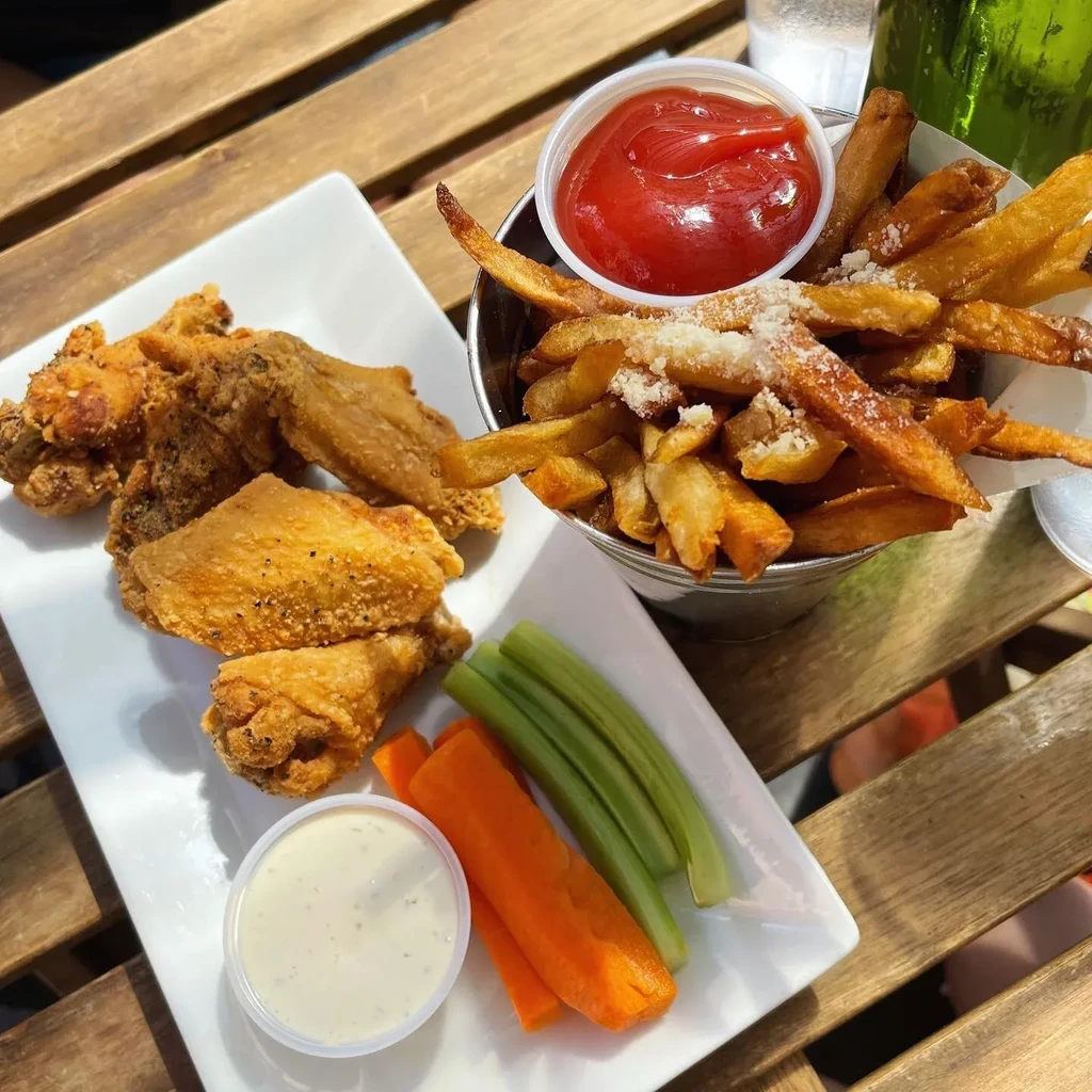 Fried chicken wings, fries with ketchup, and vegetable sticks with dip.