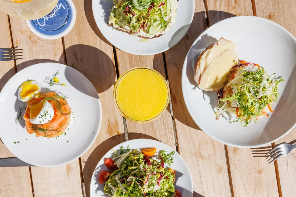 Overhead view of several plates of food, drinks, and utensils on a wooden table.