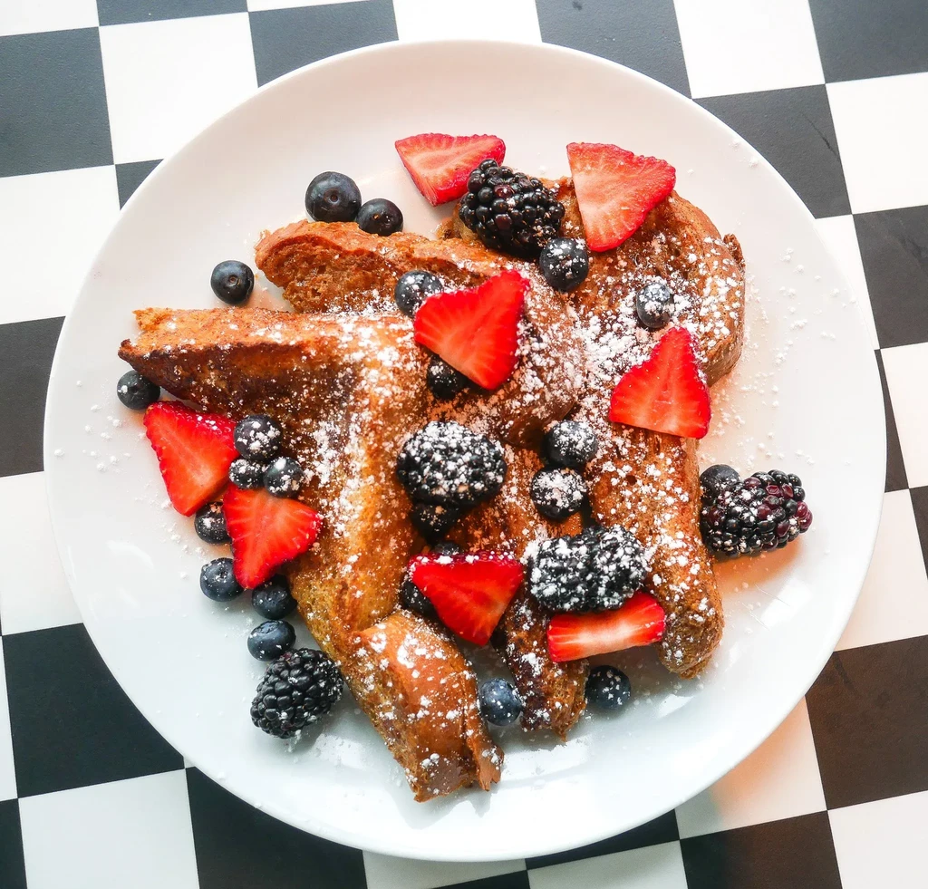 French toast with powdered sugar, strawberries, blueberries, and blackberries on a white plate.