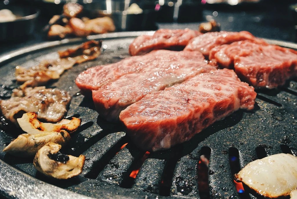 Raw meat and mushrooms cooking on a hot grill.