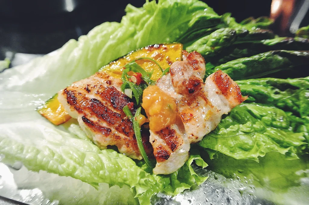 Grilled meat and squash with sauce on a bed of green lettuce.