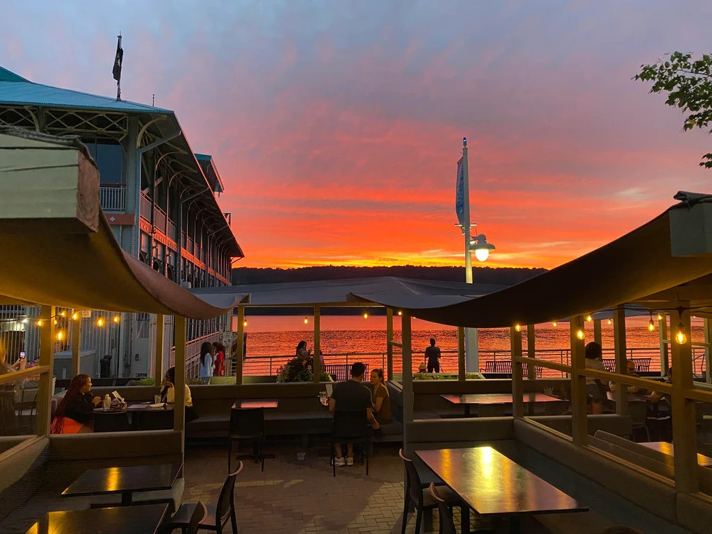 People dine on a patio overlooking a lake at sunset.