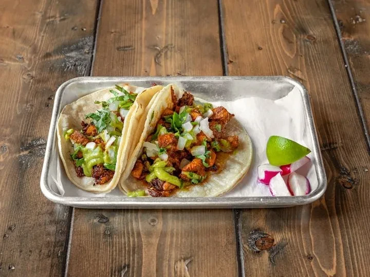 Two tacos with chicken, salsa verde, onions, and lettuce on a metal tray.