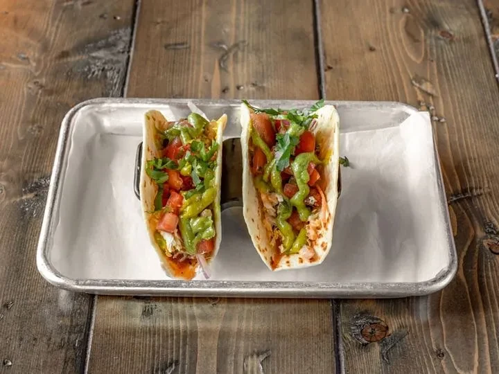 Two full tacos with green sauce and red toppings on a tray.
