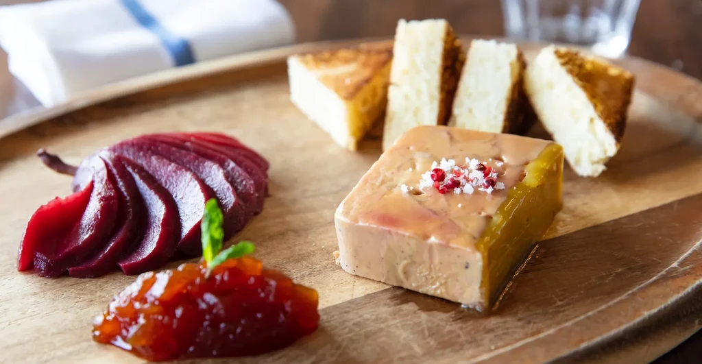 Foie gras with sliced pear, chutney, and toasted brioche on a wooden board.
