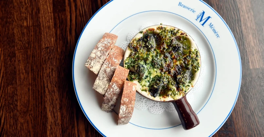 Escargot in a small skillet with bread slices on a white plate.