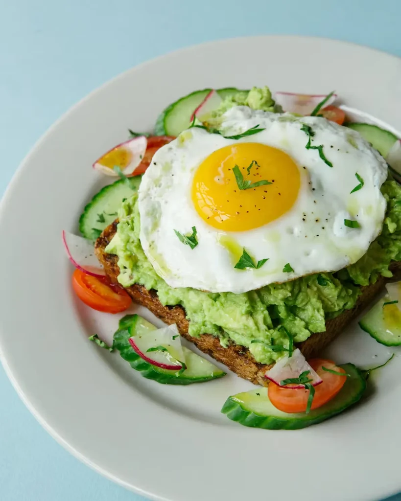 Avocado toast with fried egg, cucumbers, radishes, and tomatoes.