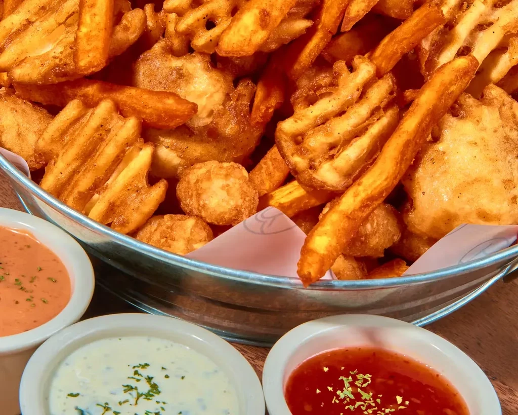 A bucket of fries, waffle fries, and tots with three dipping sauces.