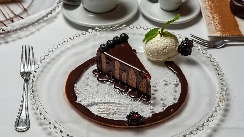 Chocolate cake slice with blueberries, ice cream, and blackberries on a plate.