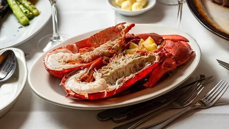 Cooked lobster halves with lemon wedges on a white oval plate.
