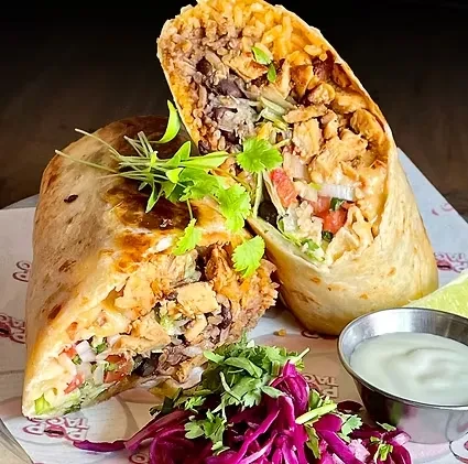 Two cut burritos with meat, rice, and vegetables, garnished with cilantro.