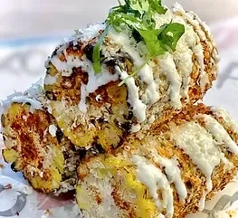 Roasted corn covered in cheese, cilantro, and white sauce.