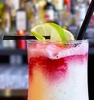 A layered red and white blended cocktail with lime slices and a straw.