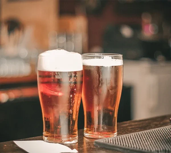Two glasses of golden beer with foamy heads on a bar.