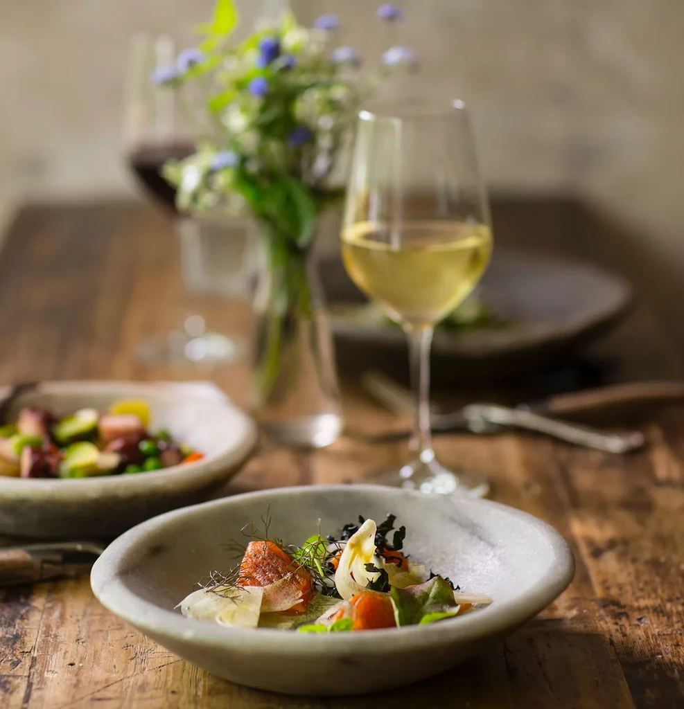 Two small bowls of gourmet food and wine on a rustic wooden table.