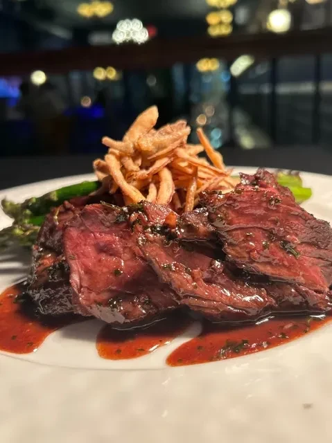 Sliced steak with sauce, asparagus, and fried onions on a plate.