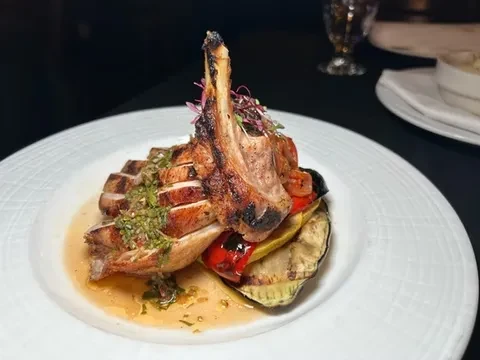 Grilled pork chop with vegetables and sauce on a white plate.