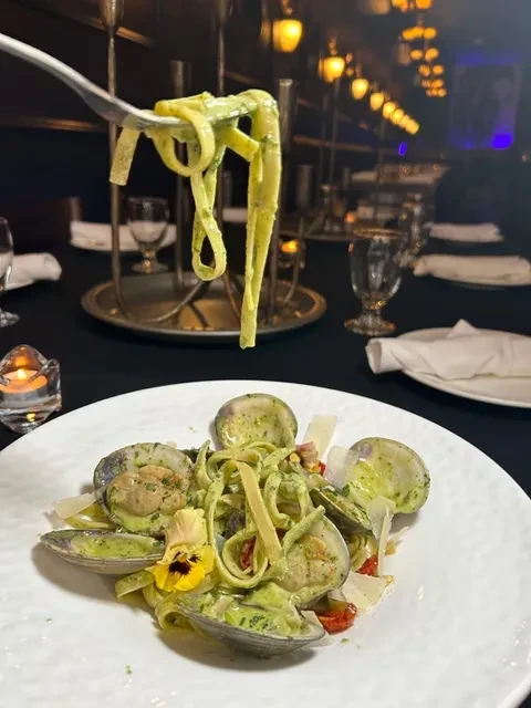 Fork lifts green pasta from a plate of clams and cheese.
